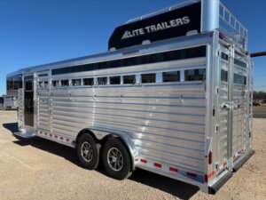 A large silver Elite 4+1 Combo livestock trailer with two axles and black-topped branding reading ELITE TRAILERS is parked on gravel under a clear sky. The trailer features multiple vents, a rear loading door, and convenient Side Tack storage. -Stillwater Trailer Sales