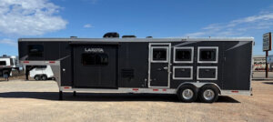 A large black Lakota horse trailer with multiple windows and compartments, parked on a gravel lot under a blue sky with scattered clouds. -Stillwater Trailer Sales