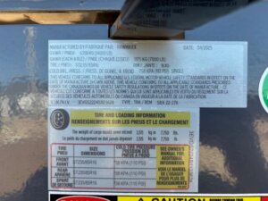 A close-up of a Swift Built manufacturer label on equipment, showing specifications such as weight ratings, tire size, pressure, and safety warnings in both English and French. The label includes numbers, dates, and reference codes for the Tack Box Combo. -Stillwater Trailer Sales