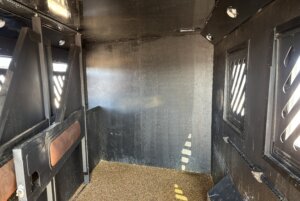 The interior of this Alumi Tech horse trailer features padded dividers, textured flooring, and vented windows with metal bars for ventilation. The space appears clean and well-lit. -Stillwater Trailer Sales