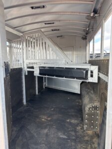 Interior of an empty horse trailer with metal dividers, padded side panels, and a black padded divider in the center, designed for transporting animals safely. -Stillwater Trailer Sales
