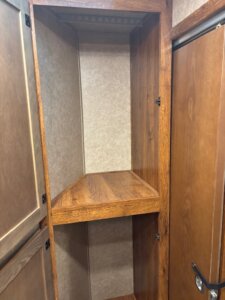 A wooden pantry cabinet with a single shelf, empty, situated between two closed doors in a room with brown walls and wood trim. -Stillwater Trailer Sales