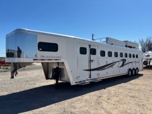 A large white gooseneck horse trailer with multiple windows and black swoosh designs is parked on gravel under a clear blue sky. -Stillwater Trailer Sales