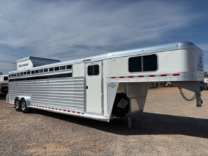 An Elite 8 Horse Trailer, featuring a silver gooseneck design with side vents and tandem axles, is parked on gravel under a blue sky&mdash;perfectly suited for hauling animals. -Stillwater Trailer Sales