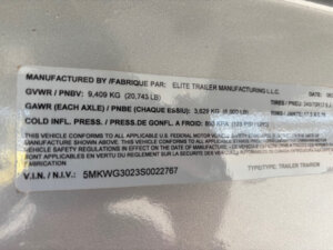 Close-up of a metallic label on an Elite 8 Horse Trailer, displaying manufacturing details, weight capacities, tire pressure information, and a VIN number. Text is printed in both English and French. -Stillwater Trailer Sales