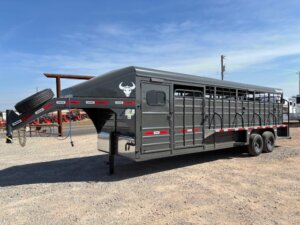 A large black livestock trailer with a gooseneck hitch and dual axles is parked on gravel. It has a spare tire mounted on the front, side gates, and red and white reflective tape along the sides. -Stillwater Trailer Sales