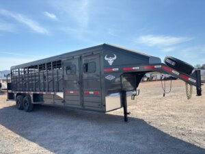 A large gray livestock trailer with a gooseneck hitch, dual axles, and red-and-white reflective tape is parked on gravel. The trailer has ventilation slats and a bull head logo on the front. -Stillwater Trailer Sales