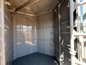Interior view of an empty Swift Built stock trailer with a gray, textured floor and smooth, reflective walls. Light enters from the open bumper pull door, casting shadows inside the trailer. -Stillwater Trailer Sales