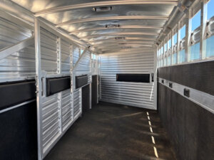 Interior of an empty, clean Elite 10 Horse Trailer with metal walls, rubber mat flooring, and barred windows letting in sunlight from the right side. -Stillwater Trailer Sales