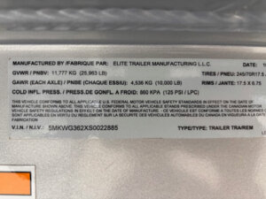 Close-up photo of an Elite 10 Horse Trailer information label showing details like manufacturer, weight limits, tire size, and VIN. Key specs include GVWR: 25,963 lbs, GAWR: 10,000 lbs/axle, and tire size: 245/70R17.5. -Stillwater Trailer Sales