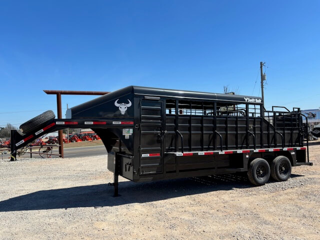 A black Swift Built gooseneck livestock trailer with a bull logo is parked on gravel near a road, under a clear blue sky. This 20' 3/4 Top trailer features multiple gates, dual axles, tack boxes, and a spare tire mounted on the front. -Stillwater Trailer Sales