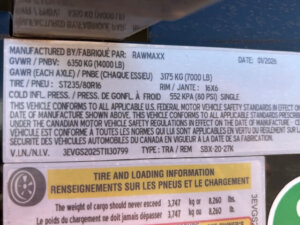 A manufacturer label on the Swift Built 20' trailer shows specs such as GVWR 6350 kg (14000 lb), GAWR 3175 kg (7000 lb), tire size ST235/80R16, rim 16x6, and cold inflation pressure 552 kPa (80 PSI). -Stillwater Trailer Sales