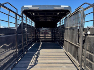 Interior view of an empty Swift Built 20' 3/4 Top black livestock trailer with open side and back gates, featuring metal railings, a wooden floor, and handy tack boxes&mdash;all shown beneath a clear blue sky. -Stillwater Trailer Sales