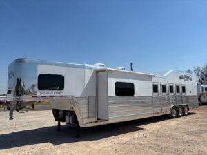 A large, silver and white horse trailer with living quarters, multiple windows, a side slide-out, and three axles is parked on gravel under a clear blue sky. The trailer reads THE EVOLUTION and 4 STAR TRAILERS. -Stillwater Trailer Sales