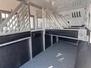 Interior of a Bloomer horse trailer with padded dividers, non-slip flooring, and individual stalls separated by metal bars, designed to safely transport multiple horses. -Stillwater Trailer Sales