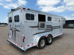 A silver Elite 3 Horse Trailer with black and red stripes is parked on gravel. It features multiple windows, rear doors, a side vent, a quote on the side, and the brand name Elite Trailers near the roof. -Stillwater Trailer Sales