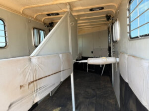 Interior of a Hawk 2+1 horse trailer with padded dividers, barred windows, and a wooden floor. The GN horse trailer is clean but shows some wear, including a visible stain on the left divider. -Stillwater Trailer Sales