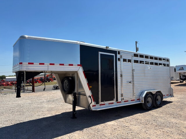 A silver and black Frontier Stock Combo gooseneck livestock trailer, 20' long with two axles, is parked on a gravel lot under a clear blue sky. The trailer features side vents, a door, and red-and-white reflective tape along the sides. -Stillwater Trailer Sales