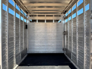Interior view of a Frontier Stock Combo 20' livestock trailer, featuring ribbed aluminum walls, a black rubber floor, and a closed center divider gate under bright daylight. -Stillwater Trailer Sales
