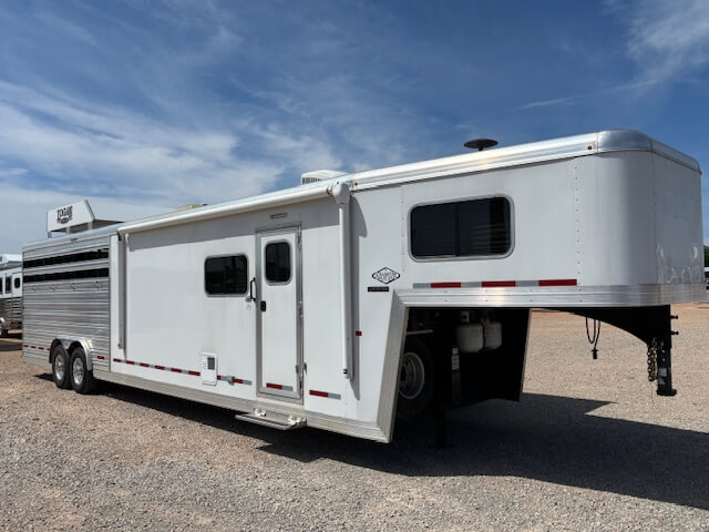 A large white Logan Stock Combo livestock trailer with living quarters is parked on a gravel lot under a partly cloudy sky. -Stillwater Trailer Sales