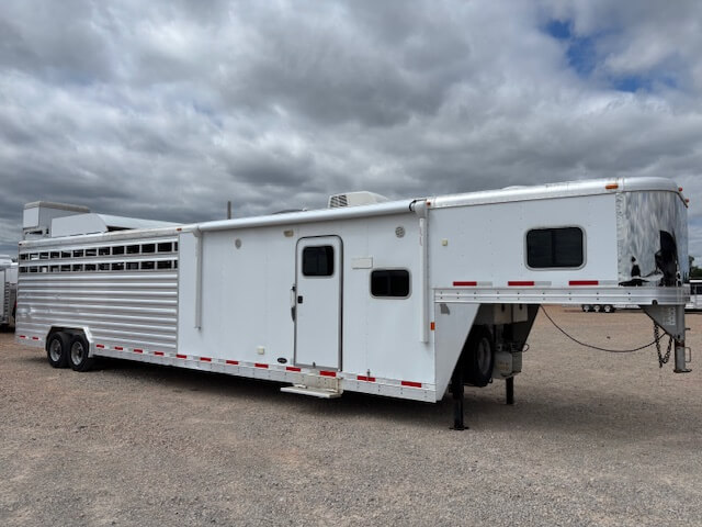 A large white Exiss Stock Combo gooseneck livestock trailer with multiple windows and vents is parked on a gravel lot under a cloudy sky. -Stillwater Trailer Sales