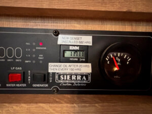 A close-up of a Sierra Custom Interiors control panel in an Exiss Stock Combo, showing a generator hour meter at 1711.1 hours, a 3/4 full fuel gauge, and labels for oil changes and genset installation. -Stillwater Trailer Sales