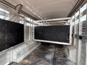Interior view of an empty Exiss Stock Combo livestock trailer with metal walls, black divider gates, and a non-slip floor. The clean, well-lit space shows sections for separating animals during transport. -Stillwater Trailer Sales