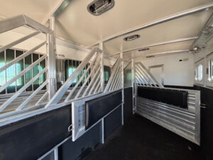 Interior of a Cimarron horse trailer with metal stalls and partitions, black and white walls, windows with bars, and overhead lights. The clean, organized space is designed for transporting up to 6 horses in comfort. -Stillwater Trailer Sales