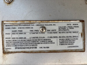 A metal manufacturer&rsquo;s label on this Cimarron 4 Horse Trailer displays specifications, including manufacturer Cimarron Trailers, Inc., date 05/2016, GVWR 8165 kg, GAWR 4082 kg, tire and rim info, VIN, and other technical details. -Stillwater Trailer Sales