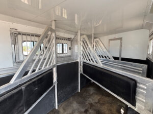 Interior of a Cimarron 4 horse trailer featuring multiple metal stalls, padded dividers, grated windows, and rubber mats on the floor, all designed for safely transporting several horses with optional living quarters for comfort. -Stillwater Trailer Sales