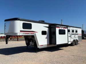A large white Bison gooseneck horse trailer with black and red accents, featuring multiple windows and doors, and 3 horse living quarters, parked on gravel under a clear blue sky. -Stillwater Trailer Sales