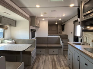 Interior of a modern Bison RV living quarters featuring a dining area with table and bench seating, a sofa, upper cabinets, kitchenette with sink and microwave, plus steps leading to a raised sleeping or storage area&mdash;ideal for 3 horse trips. -Stillwater Trailer Sales