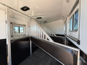 Interior of a 3 horse trailer with padded dividers, metal bars, and side windows, designed to safely transport multiple horses. Bright lighting and clean surfaces are visible, with spacious living quarters adding comfort for longer journeys. -Stillwater Trailer Sales