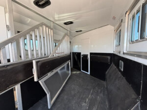 Interior of a Bison 3 Horse trailer featuring metal dividers, padded black walls, open windows with bars, and a closed white door at the far end. The rubberized floor ensures safety and comfort&mdash;ideal for travel with or without living quarters. -Stillwater Trailer Sales
