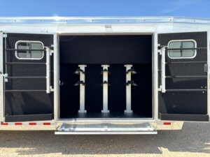 Open trailer with two rear doors showing three empty saddle racks inside, designed for transporting equestrian gear. The interior is lined with black material and two small windows are on each door. -Stillwater Trailer Sales