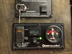 Close-up of a Bloomer 4 Horse GenSet control panel showing 1186 hours, a fuel gauge, start/stop switch, indicator lights, warning label above, and a key inserted in the HYDRAULIC ROOM EXTENSION lock&mdash;ideal for side load setups. -Stillwater Trailer Sales
