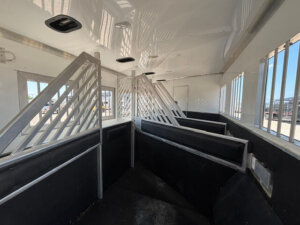Interior of a horse trailer with metal dividers and padded walls forming separate stalls, bright natural light coming through windows and vents on the ceiling. -Stillwater Trailer Sales
